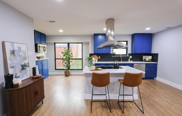6519 Club Wood, Dallas, TX 75237 - kitchen featuring blue cabinetry, island exhaust hood, stainless steel appliances, light countertops, and a kitchen bar