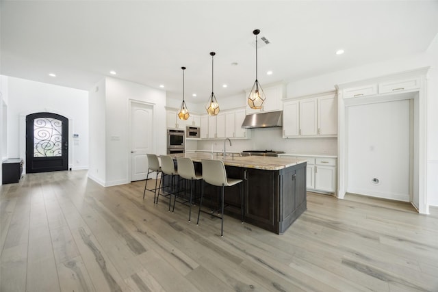 3705 Melville Cir, Flower Mound, TX 75022 - kitchen with under cabinet range hood, stainless steel double oven, white cabinetry, a large island with sink, and recessed lighting