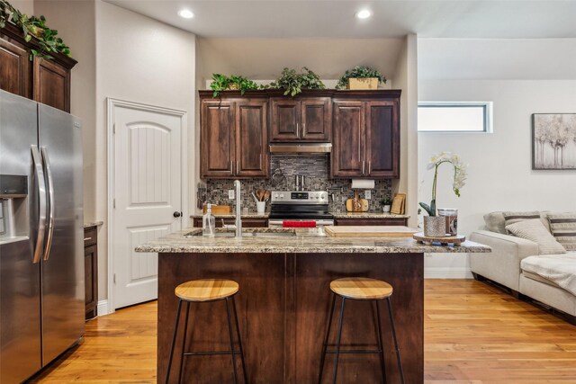 2405 La Costa Dr, Rowlett, TX 75088 - kitchen with stainless steel appliances, under cabinet range hood, light wood-style floors, a kitchen breakfast bar, and backsplash