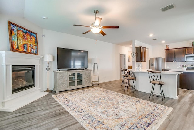 6100 True Vine Rd, Fort Worth, TX 76123 - living room featuring light wood-style flooring, a ceiling fan, a glass covered fireplace, and recessed lighting