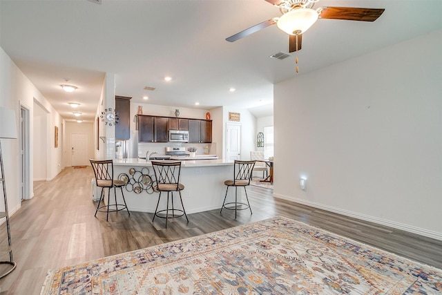 6100 True Vine Rd, Fort Worth, TX 76123 - kitchen with stainless steel appliances, dark brown cabinetry, light wood-style floors, a breakfast bar area, and light countertops