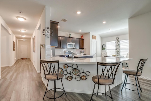 6100 True Vine Rd, Fort Worth, TX 76123 - kitchen featuring stainless steel appliances, a sink, dark brown cabinets, light wood finished floors, and a kitchen breakfast bar