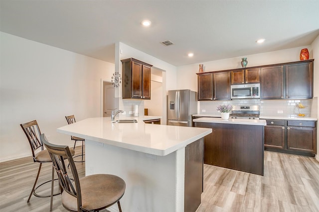 6100 True Vine Rd, Fort Worth, TX 76123 - kitchen with appliances with stainless steel finishes, a sink, light wood-style flooring, a kitchen bar, and a center island