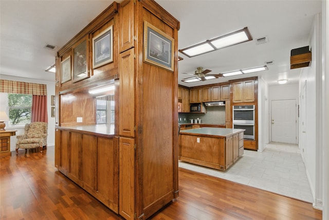 421 Olive Branch Rd, Brock, TX 76087 - kitchen featuring stainless steel double oven, brown cabinetry, ceiling fan, glass insert cabinets, and a center island