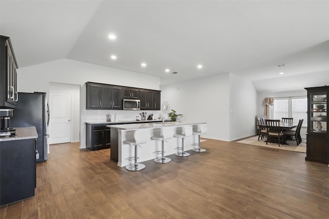 1417 Grassy Meadows Dr, Burleson, TX 76058 - kitchen featuring stainless steel appliances, a kitchen island with sink, lofted ceiling, a breakfast bar area, and dark wood-style flooring