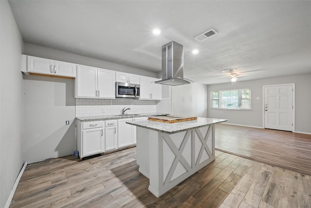 1043 Star St, Denison, TX 75020 - kitchen with stainless steel microwave, a sink, white cabinets, light wood-type flooring, and recessed lighting