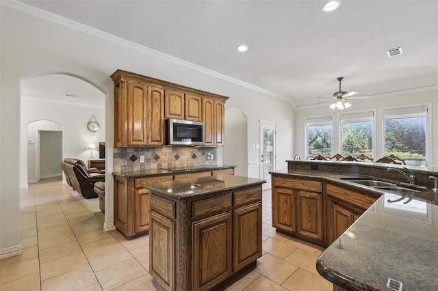 104 E Hidden Meadow Ct, Cresson, TX 76035 - kitchen featuring arched walkways, stainless steel microwave, a sink, a ceiling fan, and light tile patterned floors