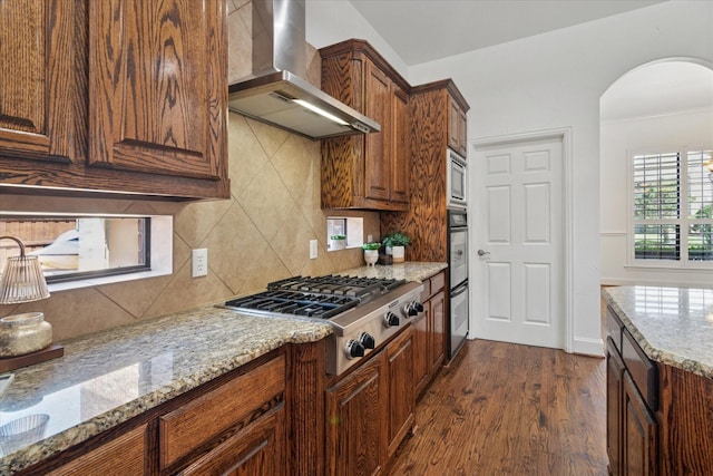 1127 Westminster Ave, Murphy, TX 75094 - kitchen featuring wall chimney range hood, appliances with stainless steel finishes, tasteful backsplash, light stone counters, and dark wood-style flooring