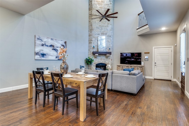 5913 Lewis St, Dallas, TX 75206 - dining room featuring a high ceiling, a ceiling fan, a stone fireplace, baseboards, and dark wood-type flooring