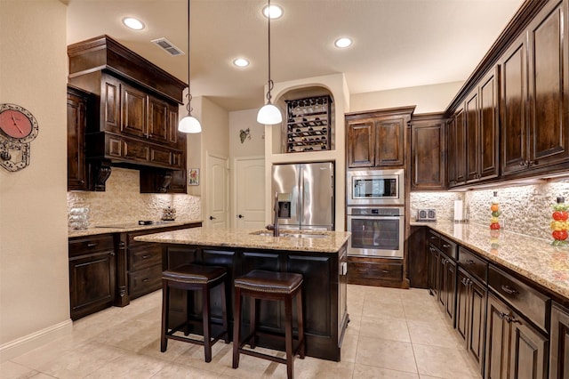 7205 E Nirvana Cir, North Richland Hills, TX 76182 - kitchen featuring stainless steel appliances, decorative backsplash, dark brown cabinetry, light stone countertops, and a center island with sink