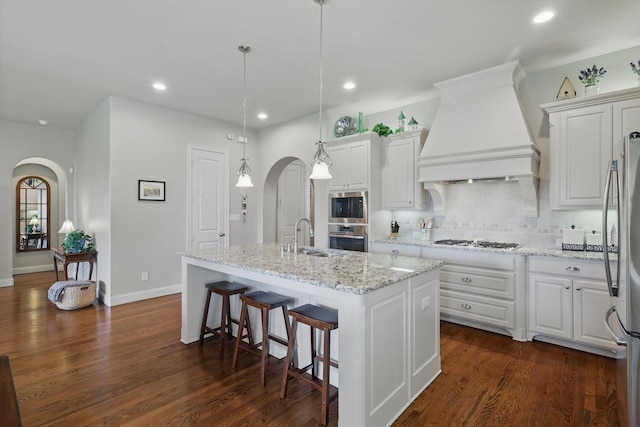 8913 Honeysuckle Dr, Lantana, TX 76226 - kitchen with arched walkways, stainless steel appliances, a sink, premium range hood, and an island with sink
