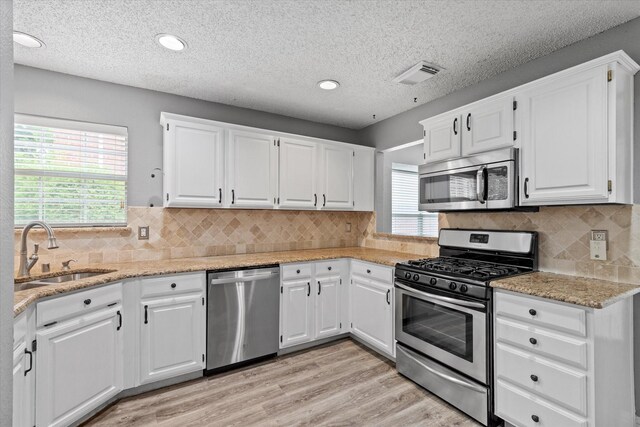 807 Fall Dr, Allen, TX 75002 - kitchen with appliances with stainless steel finishes, a sink, a textured ceiling, white cabinetry, and light wood-type flooring