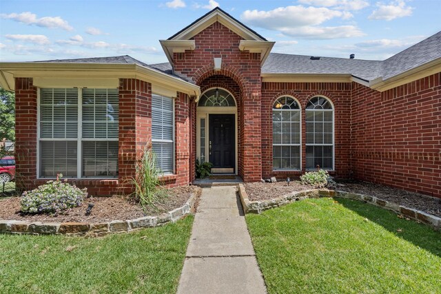 712 Saint Robby Dr, Mansfield, TX 76063 - view of exterior entry featuring brick siding, roof with shingles, and a yard