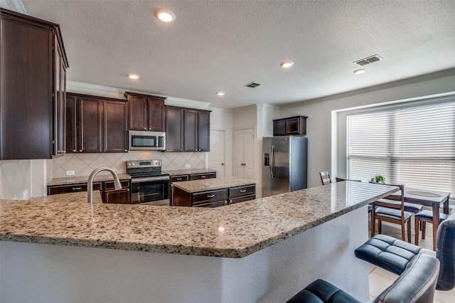 11812 Patton Dr, Frisco, TX 75036 - kitchen featuring appliances with stainless steel finishes, dark brown cabinetry, light stone countertops, decorative backsplash, and a sink