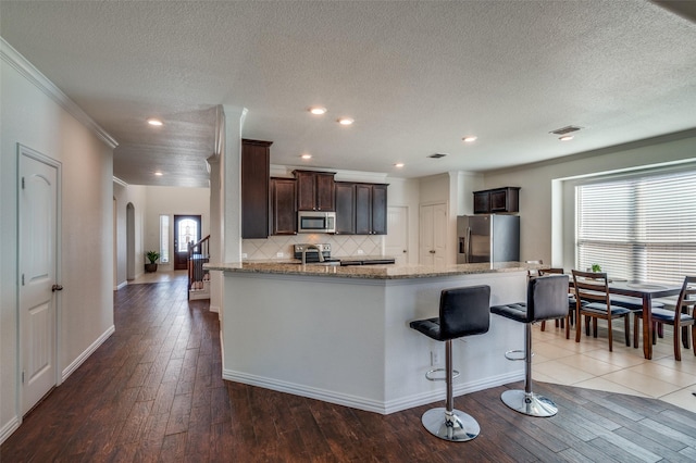 11812 Patton Dr, Frisco, TX 75036 - kitchen with appliances with stainless steel finishes, arched walkways, hardwood / wood-style floors, crown molding, and light stone counters