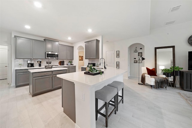 911 Bluewood St, Princeton, TX 75407 - kitchen featuring arched walkways, stainless steel microwave, gray cabinets, a breakfast bar, and recessed lighting