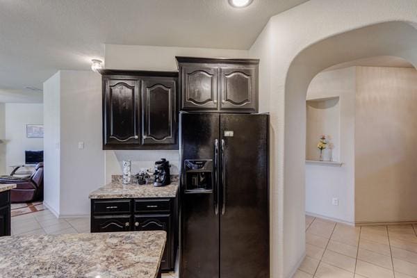 1300 Woodbine Cliff Dr, Fort Worth, TX 76179 - kitchen with black fridge, arched walkways, light tile patterned floors, light stone counters, and baseboards