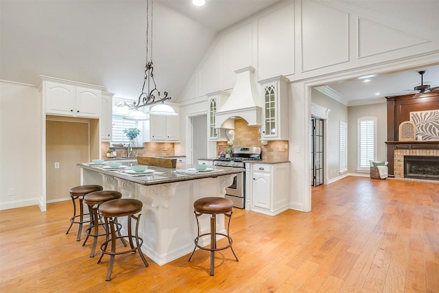 5800 Montford Dr, Colleyville, TX 76034 - kitchen with stainless steel range with gas stovetop, custom exhaust hood, white cabinetry, glass insert cabinets, and a breakfast bar