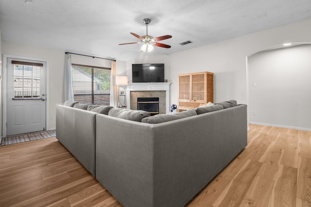 7612 Brittany Pl, Fort Worth, TX 76137 - living area featuring a ceiling fan, a tiled fireplace, light wood finished floors, arched walkways, and a textured ceiling