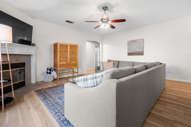7612 Brittany Pl, Fort Worth, TX 76137 - living room featuring arched walkways, ceiling fan, a tiled fireplace, wood finished floors, and baseboards