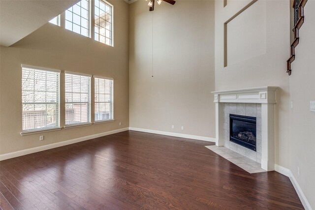 6101 Eagle Nest Dr, Garland, TX 75044 - unfurnished living room featuring wood finished floors, healthy amount of natural light, a tiled fireplace, a ceiling fan, and a towering ceiling