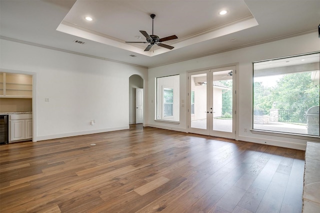 6005 Selkirk Ct, Cleburne, TX 76033 - unfurnished living room featuring a raised ceiling, healthy amount of natural light, ornamental molding, hardwood / wood-style floors, and arched walkways