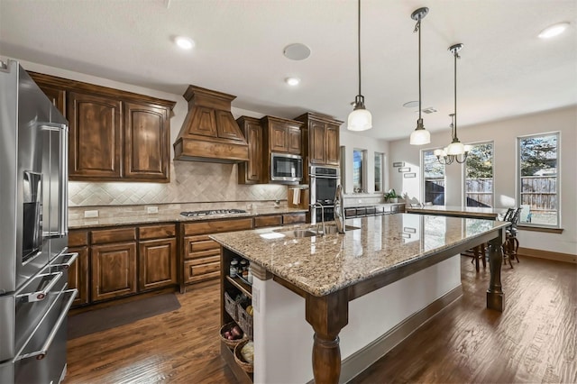 13818 Mammoth Cave Ln, Frisco, TX 75035 - kitchen with appliances with stainless steel finishes, premium range hood, a sink, decorative backsplash, and a center island with sink