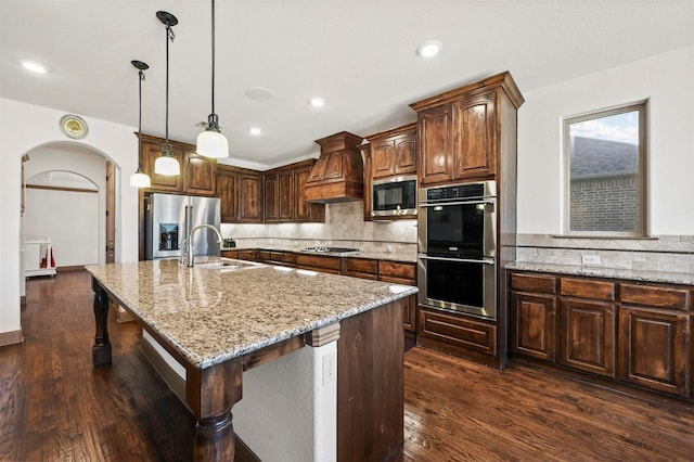 13818 Mammoth Cave Ln, Frisco, TX 75035 - kitchen with appliances with stainless steel finishes, premium range hood, arched walkways, tasteful backsplash, and light stone counters