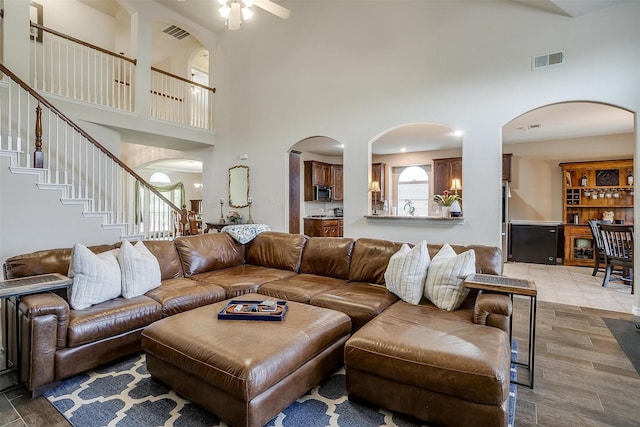 5040 Pallas Ct, Fort Worth, TX 76123 - living room featuring a towering ceiling, arched walkways, stairway, a ceiling fan, and light wood-style floors