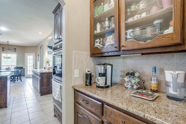 5040 Pallas Ct, Fort Worth, TX 76123 - bar featuring backsplash, arched walkways, light tile patterned flooring, stainless steel double oven, and a chandelier