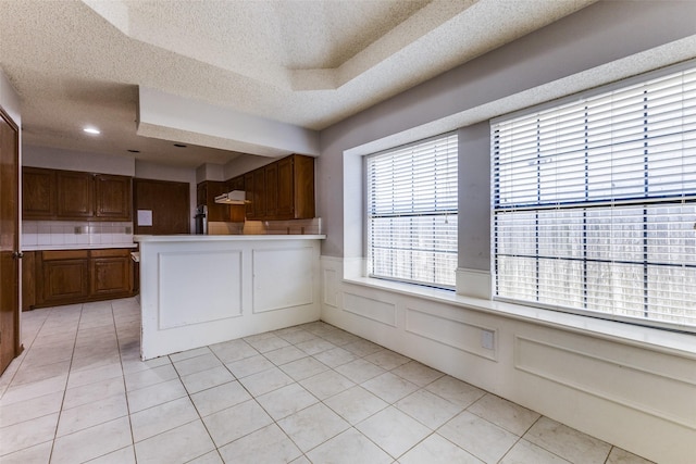 18609 Crownover Ct, Dallas, TX 75252 - kitchen featuring a textured ceiling, a wainscoted wall, a peninsula, light countertops, and light tile patterned flooring