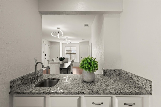 1646 Belltower Dr, Lewisville, TX 75067 - kitchen featuring a sink, a textured wall, white cabinetry, stone counters, and wood finished floors