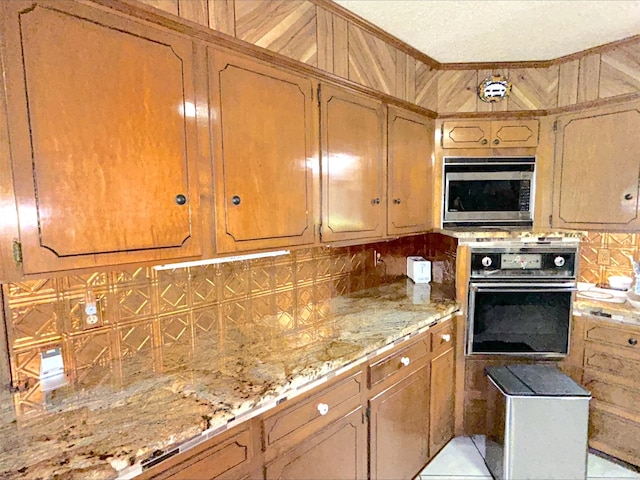 21363 Stevenson Rd, Frankston, TX 75763 - kitchen featuring stainless steel microwave, oven, tasteful backsplash, light stone countertops, and brown cabinets