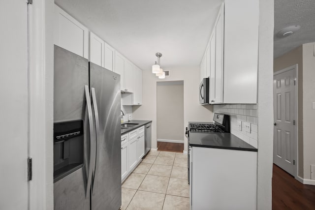 7201 Winchester Rd, North Richland Hills, TX 76182 - kitchen featuring appliances with stainless steel finishes, dark countertops, a sink, white cabinetry, and a textured ceiling