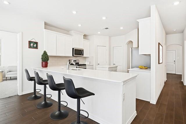 11216 Ponderosa Trl, Aubrey, TX 76227 - kitchen with stainless steel appliances, dark wood-style floors, a peninsula, decorative backsplash, and light countertops