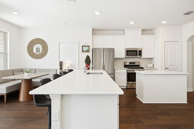 11216 Ponderosa Trl, Aubrey, TX 76227 - kitchen featuring stainless steel appliances, a center island with sink, a sink, dark wood-style floors, and backsplash
