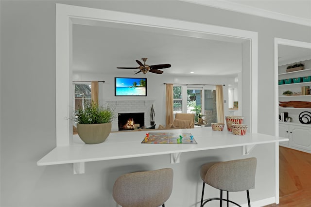 205 N College St, Mckinney, TX 75069 - kitchen featuring a brick fireplace, wood finished floors, a breakfast bar, ceiling fan, and open floor plan