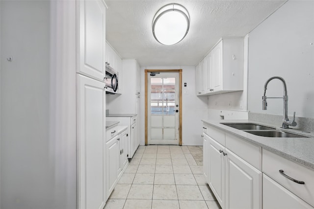 1317 Elby St, Irving, TX 75061 - kitchen with a sink, stainless steel microwave, a textured ceiling, white cabinets, and light tile patterned floors