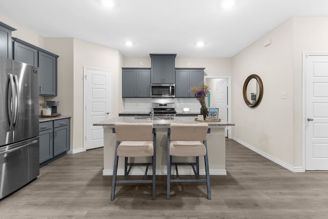 1304 Villalonga Dr, Little Elm, TX 75068 - kitchen featuring appliances with stainless steel finishes, tasteful backsplash, a kitchen breakfast bar, a center island with sink, and wood finished floors