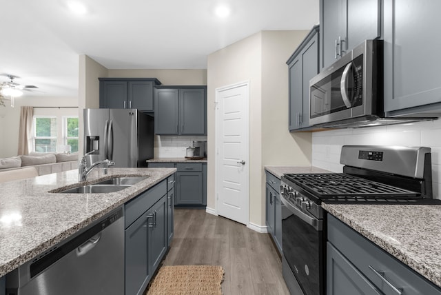 1304 Villalonga Dr, Little Elm, TX 75068 - kitchen with appliances with stainless steel finishes, a sink, decorative backsplash, wood finished floors, and light stone counters