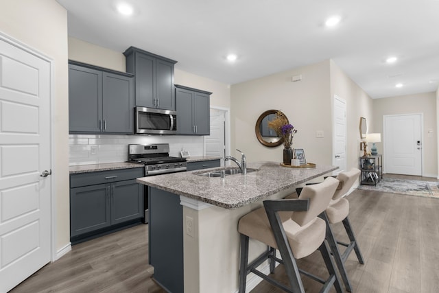 1304 Villalonga Dr, Little Elm, TX 75068 - kitchen featuring appliances with stainless steel finishes, a sink, a kitchen bar, light stone counters, and light wood-style flooring