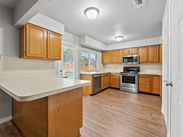 2036 Pearl Ln, Irving, TX 75060 - kitchen featuring stainless steel appliances, a peninsula, light countertops, a sink, and light wood-type flooring