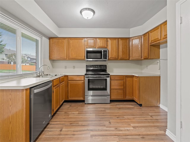 2036 Pearl Ln, Irving, TX 75060 - kitchen with appliances with stainless steel finishes, a sink, light countertops, light wood-style flooring, and brown cabinetry