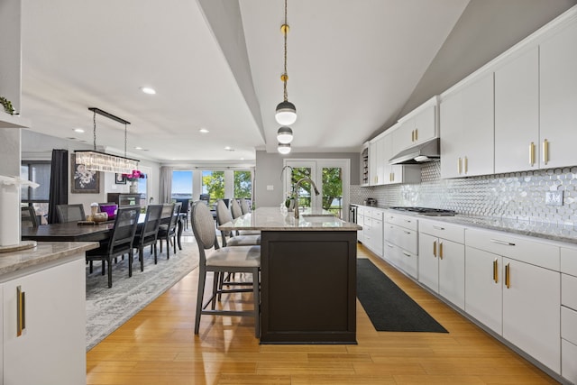 510 Columbia Dr, Rockwall, TX 75032 - kitchen with under cabinet range hood, a sink, stainless steel gas stovetop, tasteful backsplash, and white cabinetry