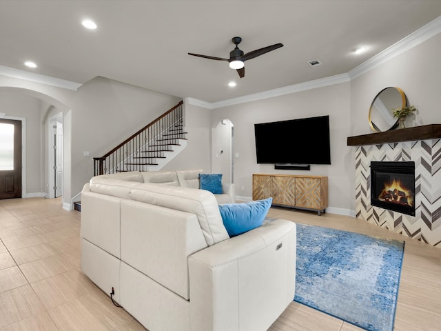 318 Arcadia Way, Rockwall, TX 75087 - living room featuring arched walkways, ceiling fan, a large fireplace, crown molding, and stairs