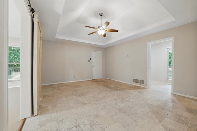 5518 Oak Branch Dr, Arlington, TX 76016 - spare room with a tray ceiling, a barn door, ceiling fan, baseboards, and light stone finish flooring