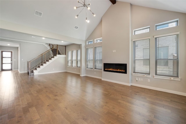 3493 Hollow Pine Dr, Frisco, TX 75033 - unfurnished living room featuring high vaulted ceiling, stairs, a glass covered fireplace, wood finished floors, and a chandelier