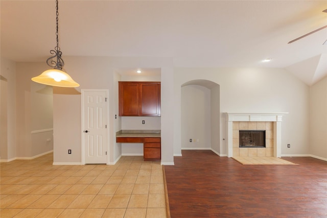 6506 Bunker Hill Ct, Rowlett, TX 75089 - unfurnished living room featuring ceiling fan, a tiled fireplace, vaulted ceiling, built in desk, and light wood finished floors