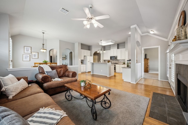 7308 Claridge Ln, Mckinney, TX 75072 - living room with lofted ceiling, a ceiling fan, arched walkways, a fireplace, and light wood-type flooring