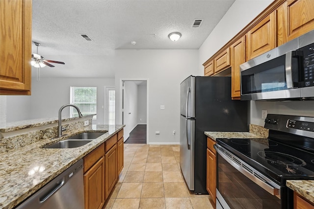 1412 Mockingbird Ln, Desoto, TX 75115 - kitchen with appliances with stainless steel finishes, a sink, brown cabinets, light stone counters, and a ceiling fan